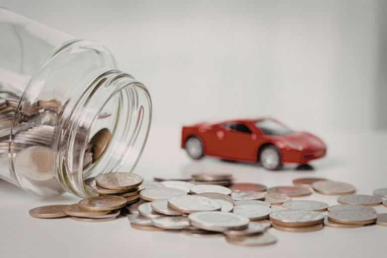 A red toy car next to a a spilled jar on pennies