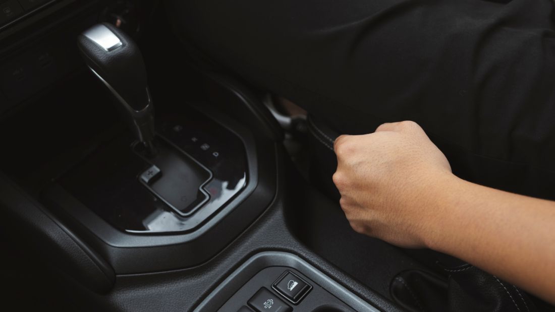 A person gripping the handbrake of a car, preparing to change gears while driving.