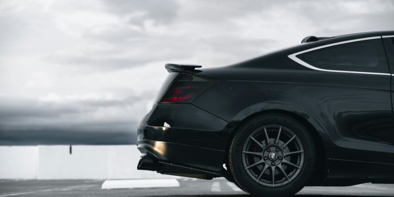 A black car parked in a parking space under a cloudy sky.