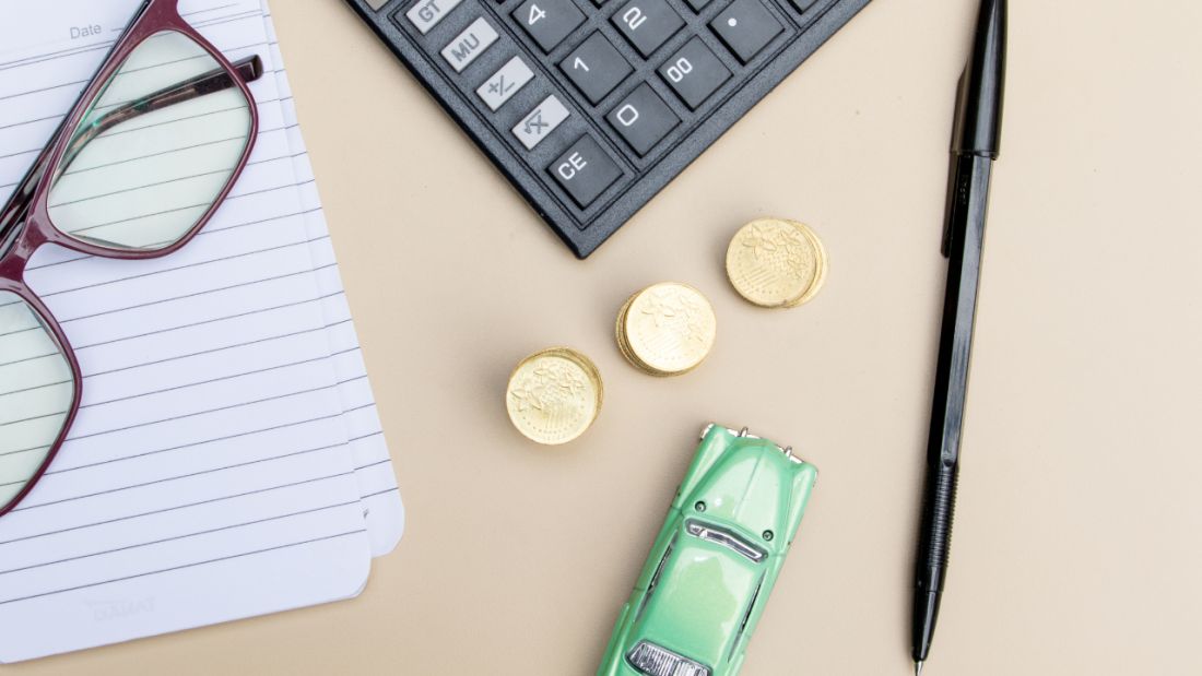 Busy desk with toy car, glasses, notepad, and calculator