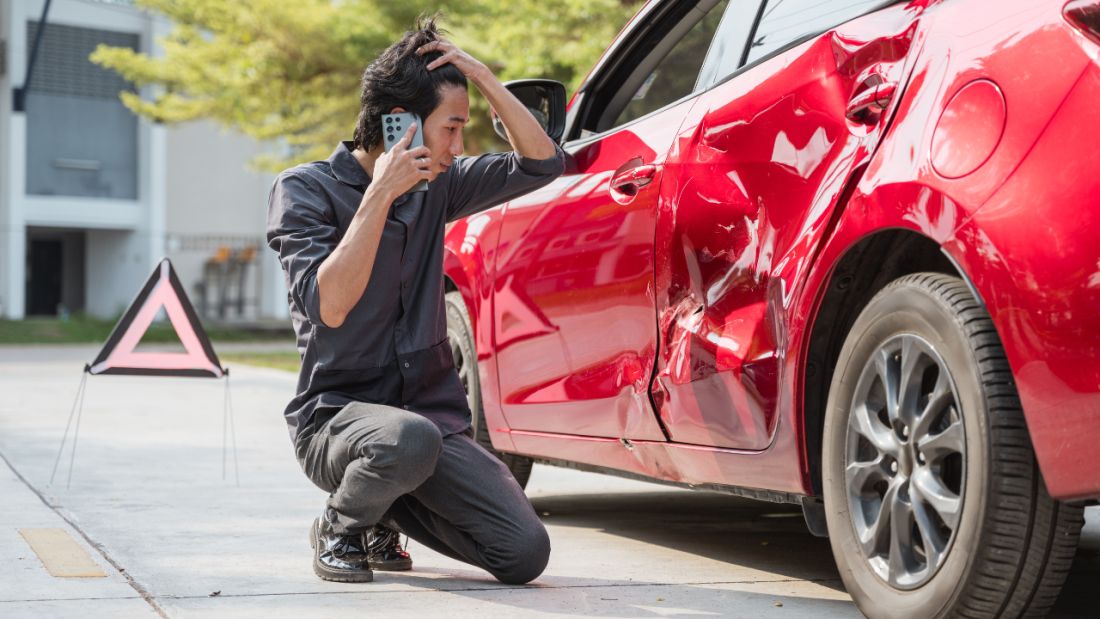 Man on phone discussing dent in red car