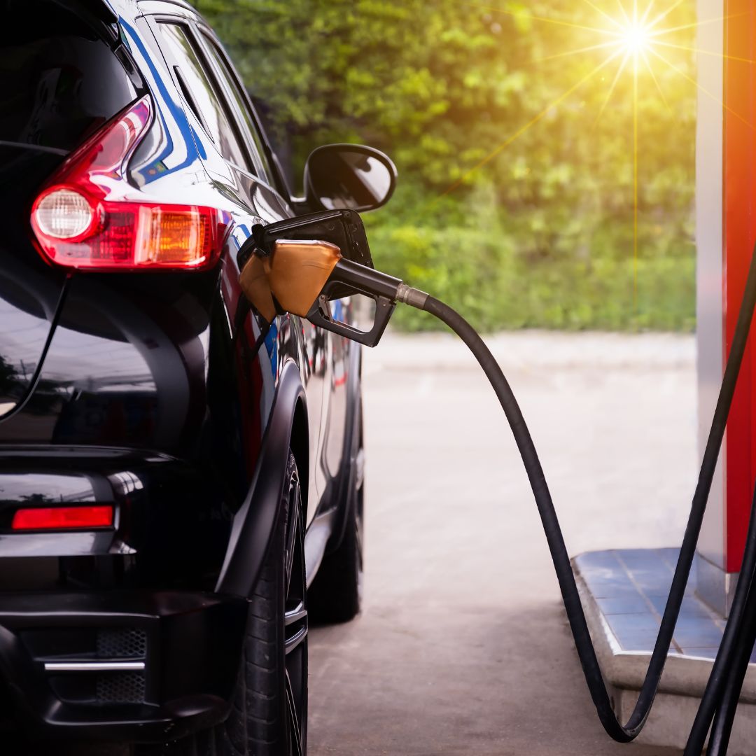 A black car being refueled at a petrol station, with a fuel pump inserted into its tank.