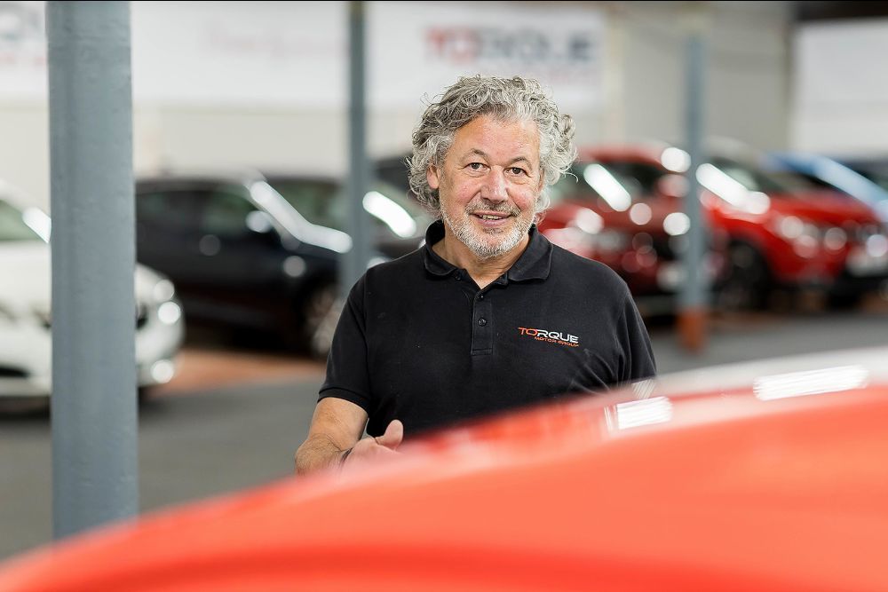 Man standing in used car showroom with vehicles in background.