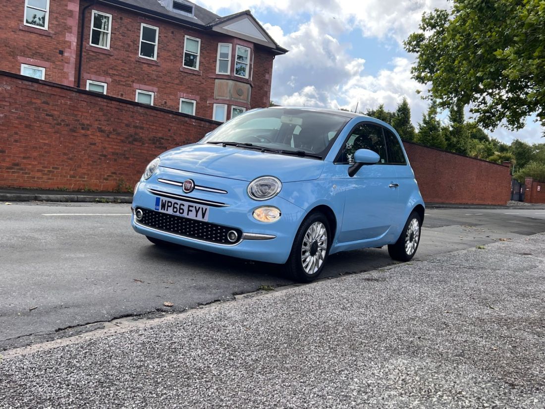 Light blue Fiat 500 parked on residential street.