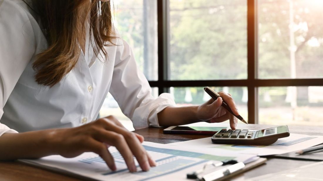 Woman using a calculator with her hand on a clipboard.