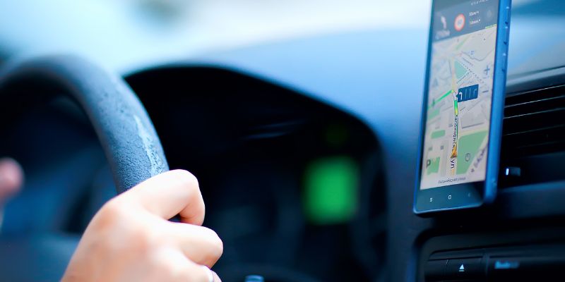 A driver holds the steering wheel of a car, with a smartphone positioned near with map directions