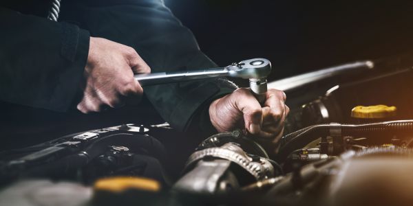 Close up on under a vehicle bonnet with a mechanics hand and a tool