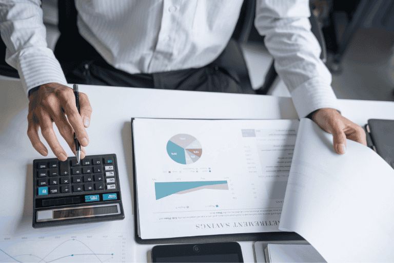 a man is sat at his desk working out his car finances with a calculator and a sheet full of graphs