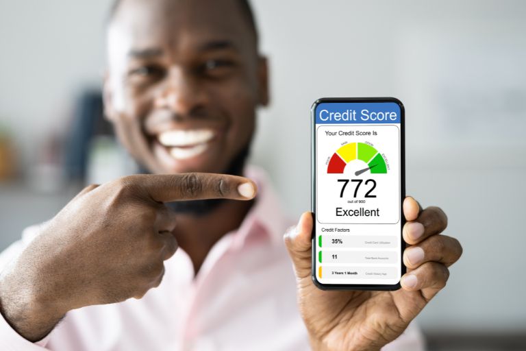 A man smiling pointing at his excellent credit score on his phone.