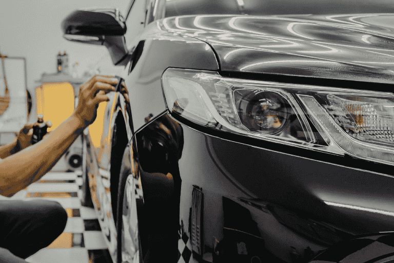 A man crouched down next to a black car checking its tyres for an MOT