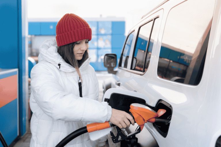 A woman in a white coat and red hat filling her car at the pump