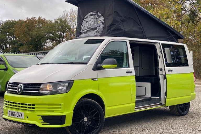 Green and white converted Volkswagen Transporter campervan. The side door is open and the collapsible roof is deployed.