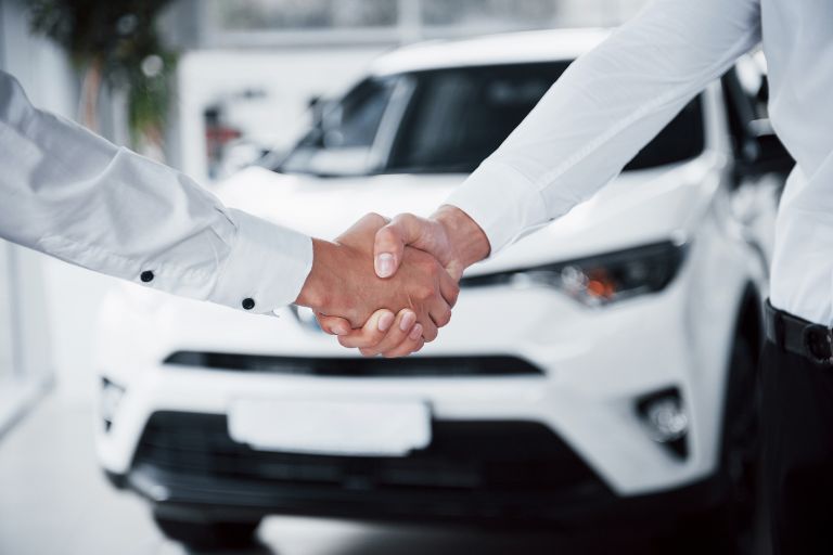 Two people shaking hands in front of a white van. 