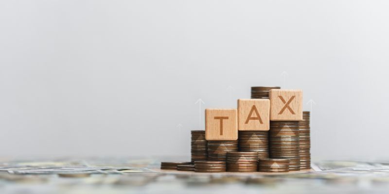 Coins Stacked Up With 3 Wooden Blocks Spelling "Tax"