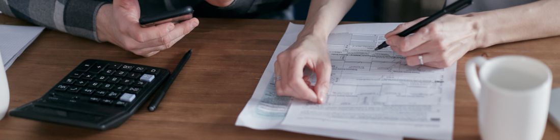 Hands signing a document on a desk with a pen and a calculator next to the paper