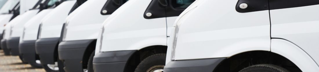 A row of white vans parked neatly in a line.