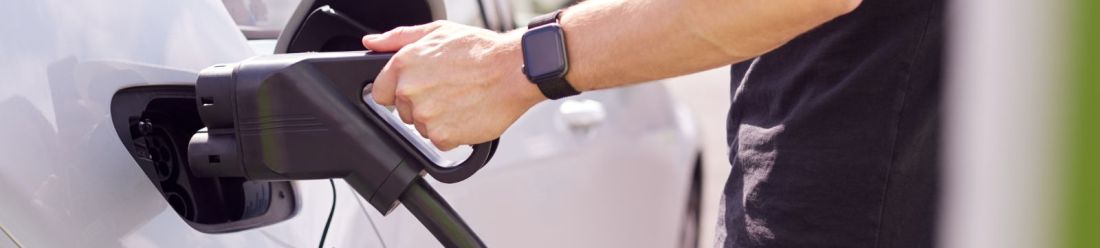A person holds a black electric car charger, ready to connect it to an electric vehicle for charging.