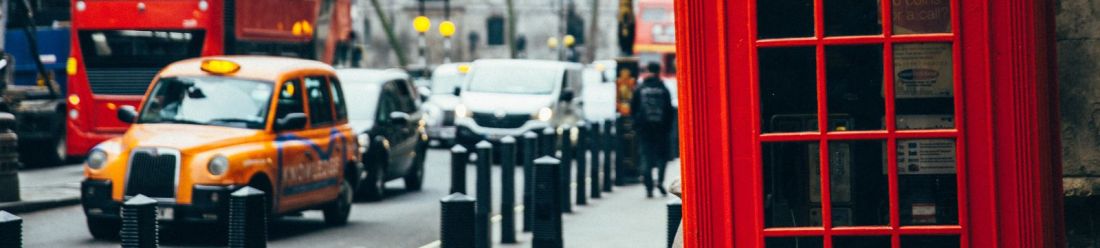 A red telephone box stands beside a classic taxi cab on a city street in London.