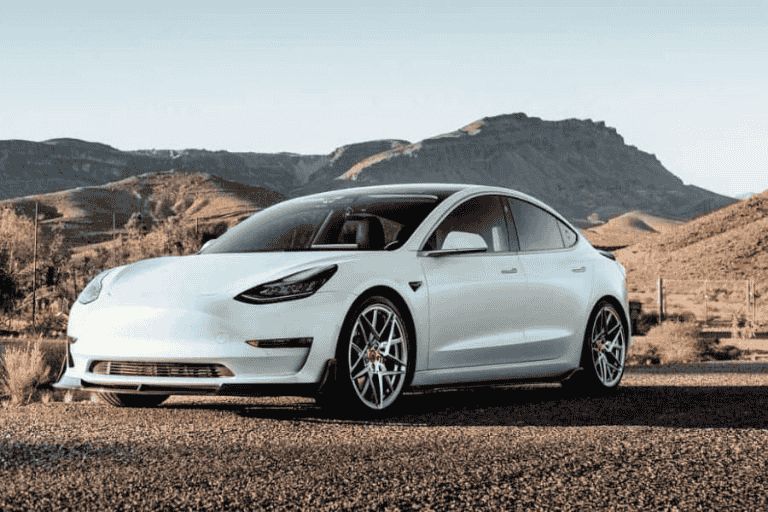 White Tesla Model 3, photographed in front of a mountain range.