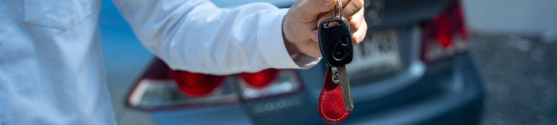 Person holding out a car key in front of a vehicle.