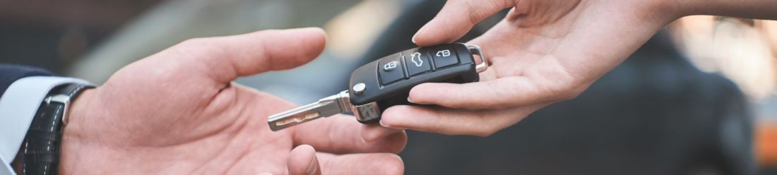 A person handing a car key to another person, symbolising the act of purchasing a vehicle.