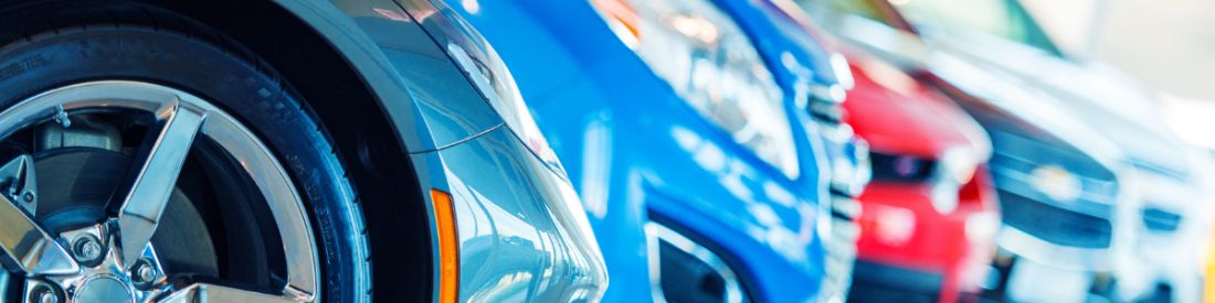 Row of colourful cars parked in a showroom, with a close-up view of a front wheel.