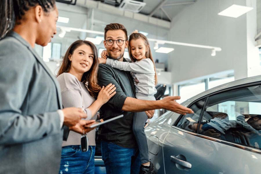 Family speaking with a sales representative while viewing a car inside a dealership.