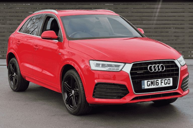 Red Audi Q3, parked in front of a brown panelled fence.