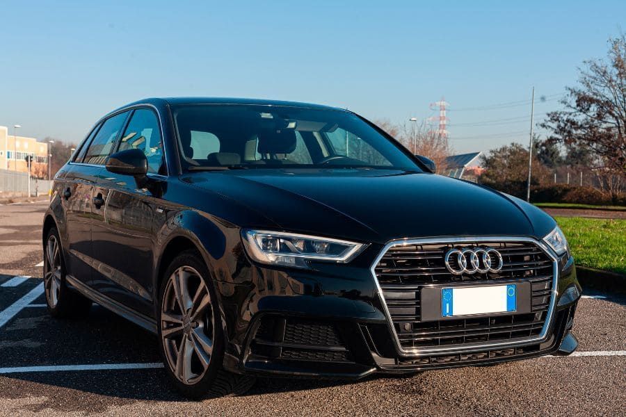 Black Audi A3 parked in a car park under a blue sky.