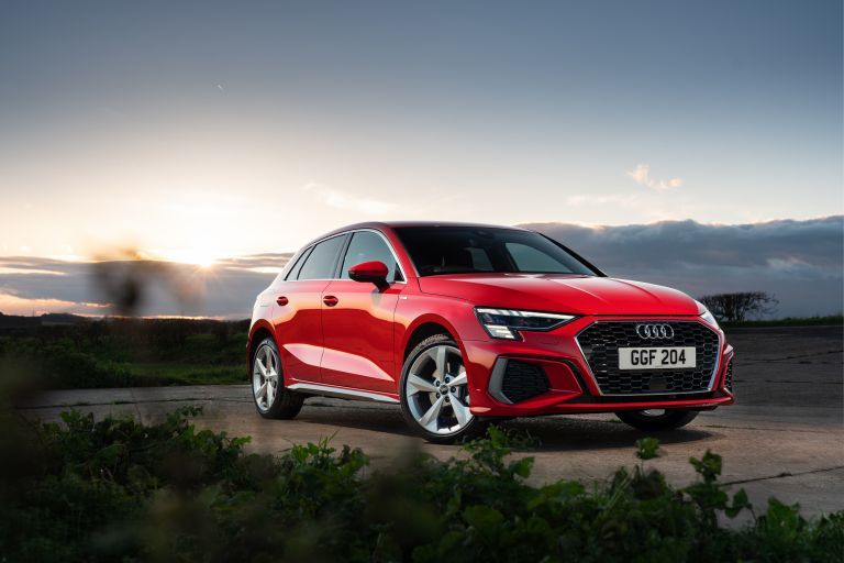Red Audi A3 parked outdoors at sunset with countryside views.