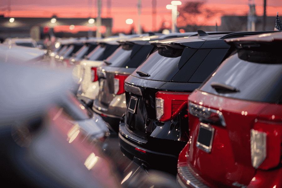 Row of parked used cars in a dealership forecourt at sunset.