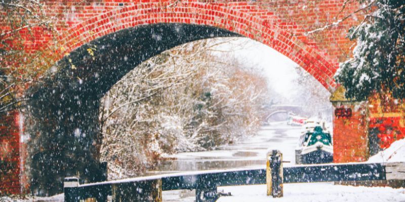 Snow-covered canal beneath a red brick bridge during winter.