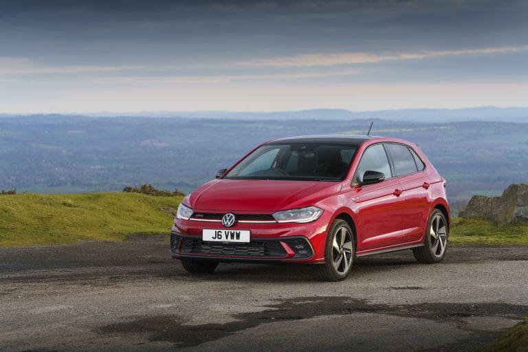 Red Volkswagen Polo parked on a hilltop road with scenic countryside views.