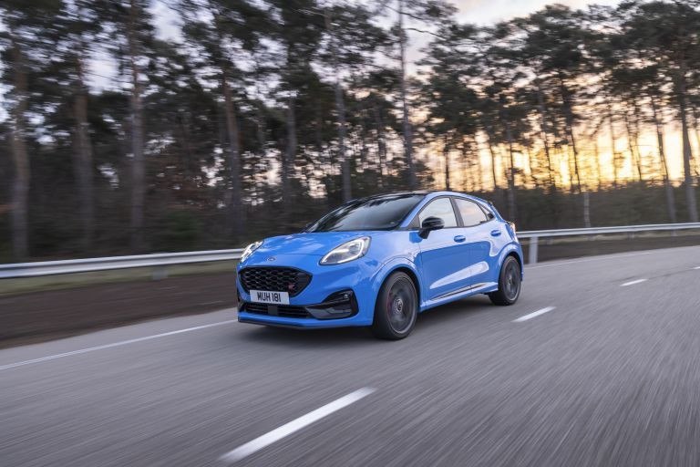 Blue Ford Puma driving on a road through a forest at sunset.