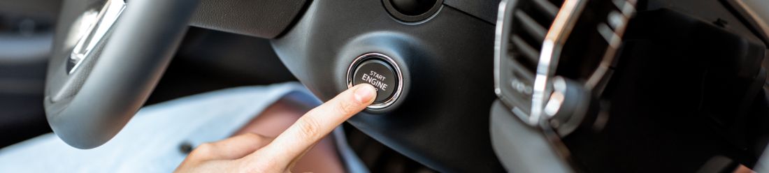 A hand pressing the 'start engine' button in a keyless car.