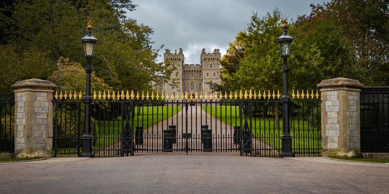 Castle viewed through black iron gates with a tree-lined pathway.