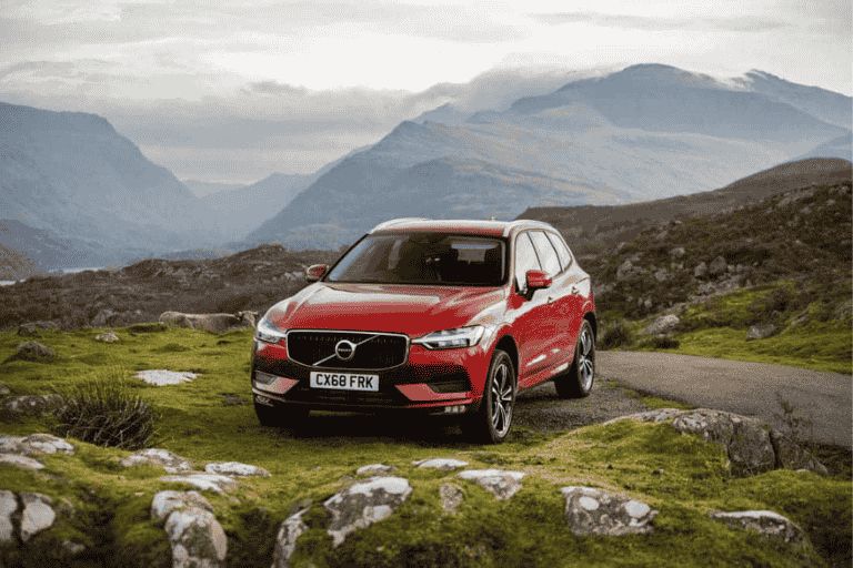 Red Volvo XC60 parked on a scenic mountain road surrounded by hills.