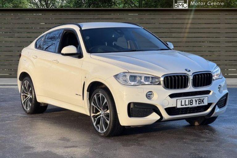 White BMW X6 SUV parked on a dealership forecourt.