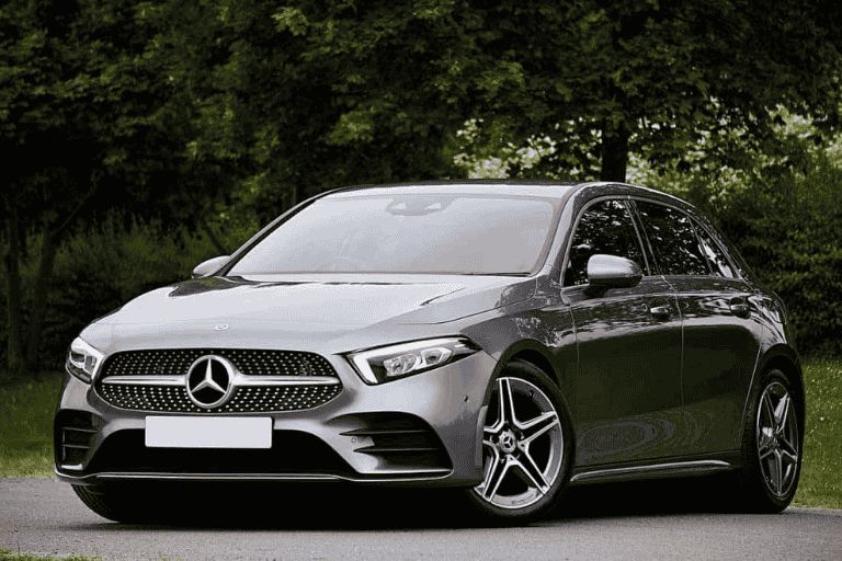 Grey Mercedes-Benz A-Class parked on a road surrounded by trees.