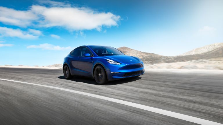 Blue Tesla Model 3 driving on an open desert road.