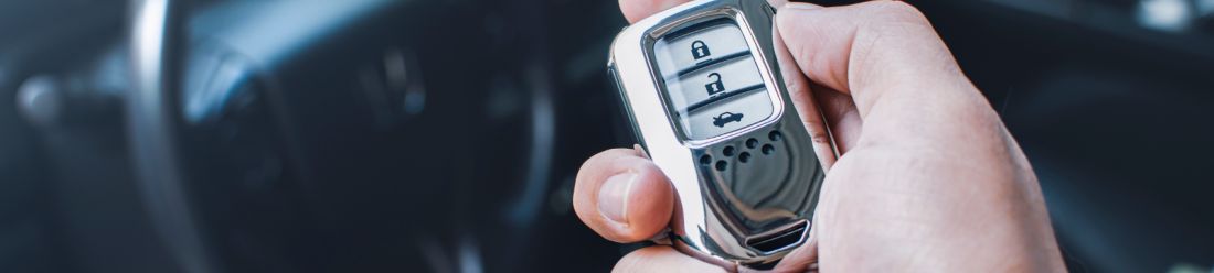Hand holding car key fob inside vehicle ready to unlock and drive away.